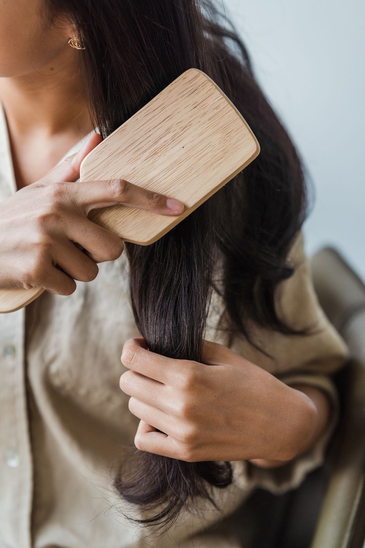 Woman brushing long hair with a wooden brush. Photo: Greta Hoffman via Pexels.