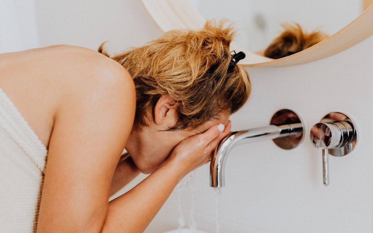 Woman washing her face at a bathroom sink during a natural morning skincare routine. Photo via Pexels.