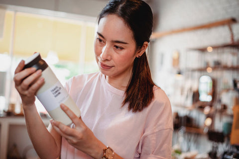 Woman reading the ingredients label on a cosmetic product. Photo: Sam Lion via Pexels.