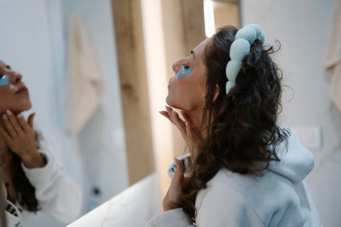 Woman applying skincare in front of a bathroom mirror