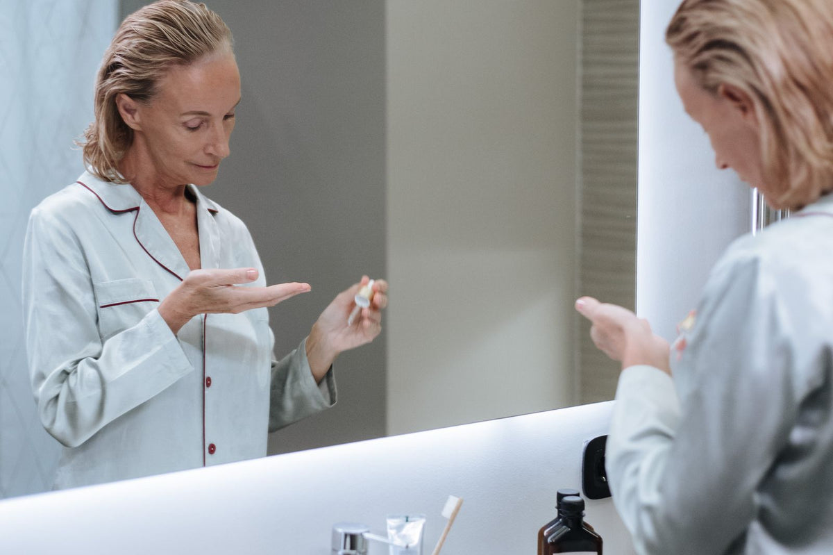 Woman applying facial serum in a mirror. Photo: Ron Lach via Pexels.