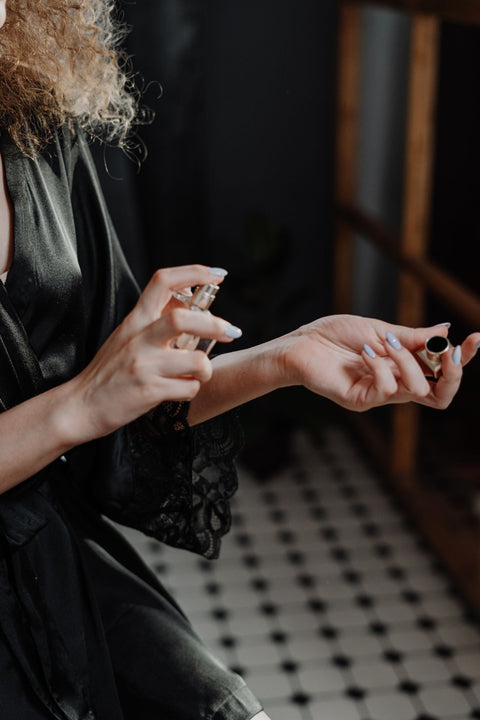 Woman wearing a silk robe and applying perfume. Photo: cottonbro studio via Pexels.