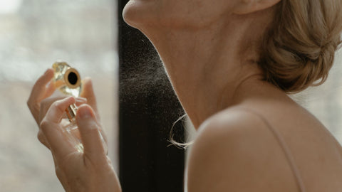 Woman applying fragrance from a glass perfume bottle in natural light, illustrating perfume scent perception. Photo via Pexels.