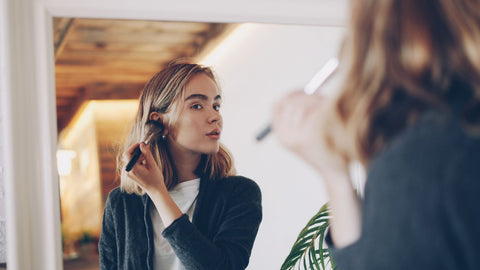 Woman applying makeup in front of mirror. Photo: Vitaly Gariev via Pexels.