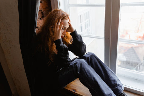 Woman sitting thoughtfully beside a window. Photo: MART PRODUCTION via Pexels.