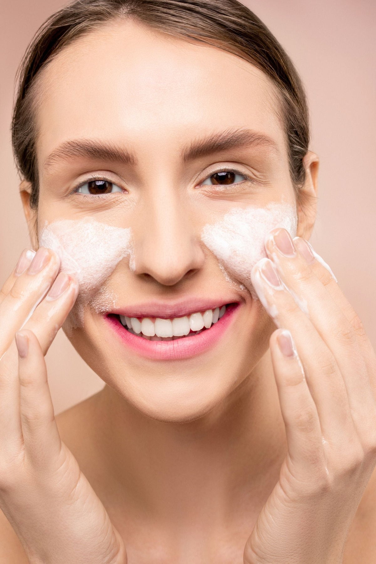 Woman washing her face with foaming cleanser, illustrating the role of surfactants in skincare.